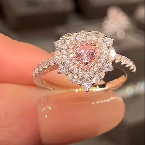 Primo piano di un anello con diamante a cuore rosa e castone halo al dito