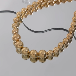 Detail view of golden chunky bead necklace with gradient beads on reflective surface