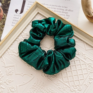Close-up of dark green metallic scrunchie with pleated texture on magazine background