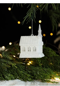Close-up of white glitter church ornament hanging on a pine tree with warm bokeh lights