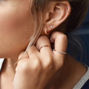 Detailed view of rose gold earring set and rings worn by a model in a minimalist style