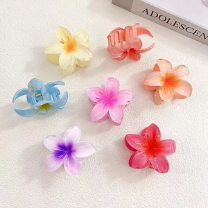 Flat lay of seven colorful gradient flower hair claws on a textured beige surface