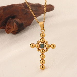 Detail of vintage gold cross pendant with green zircon center on white textured surface