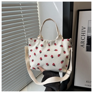 Detail of beige corduroy tote bag featuring red strawberry print and adjustable strap