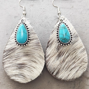 Detailed view of teardrop earrings featuring cow print fur and turquoise stone inlays