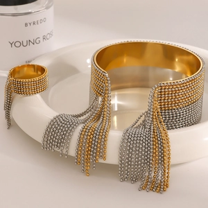 Close-up of golden stainless steel cuff bracelet and ring with long ball chain tassels