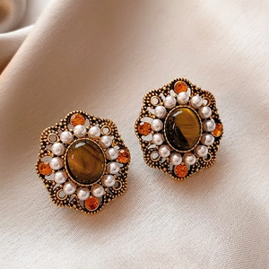 Detailed close-up of vintage gold earrings with tiger eye stone and pearls on beige fabric