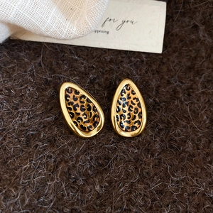 Macro shot of gold teardrop earrings with leopard print enamel on soft brown plush fabric