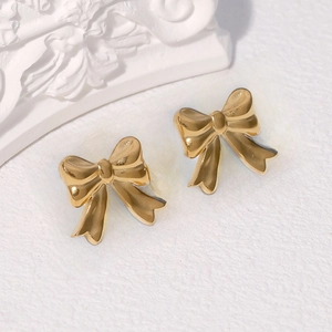 Minimalist golden bow stud earrings in stainless steel on a white textured background