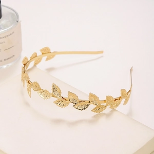 Detail of a golden metal headband featuring intricate leaf carvings on a textured base