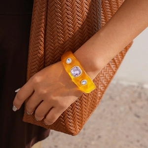 Close-up of amber resin cuff bracelet with purple rhinestone on a woven bag