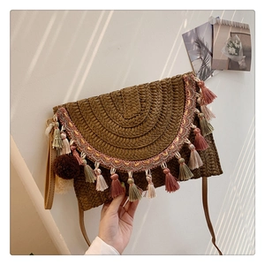 Straw bohemian shoulder bag with colorful tassels and pom poms held against a textured wall