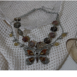 Detail of silver double-layered necklace with amber glass flower beads and crystal butterfly