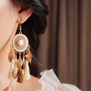 Detail of vintage bohemian tassel earrings with white enamel and leaf pendants on model