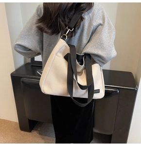 Beige canvas tote bag with black straps worn by a model in a casual daily setting