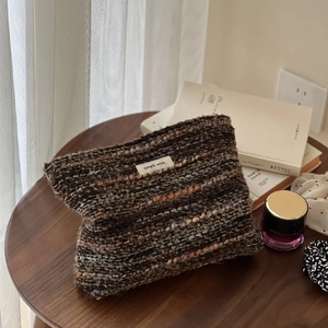 Retro tweed wool cosmetic bag with woven texture and white logo on a wooden table