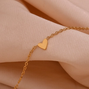 Macro detail of 18K gold plated stainless steel heart charm on a delicate chain bracelet