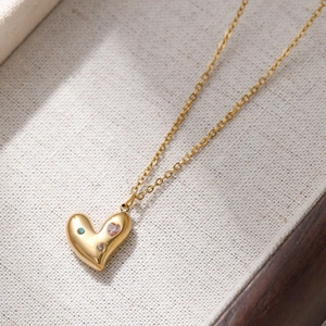 Collana con ciondolo a cuore dorato e zirconi colorati su sfondo di lino beige