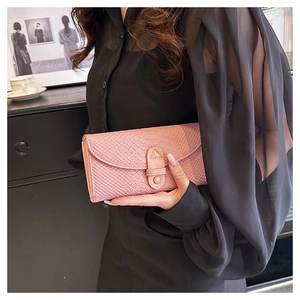 Detailed close-up of pink crocodile-embossed leather wallet held by a model in a stylish setting