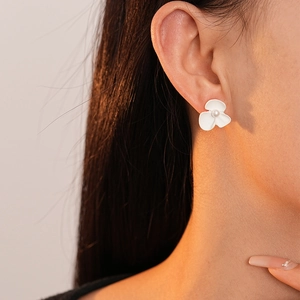 Detailed close-up of a white flower earring with a pearl center worn by a model