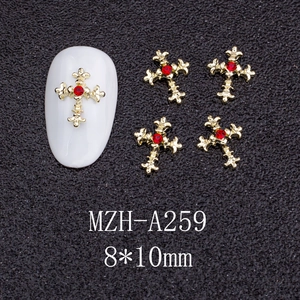 Macro detail of gold cross nail charms with red rhinestones and vintage textures