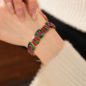 Detailed close-up of vintage gold bracelet with green enamel and pink gemstones on wrist