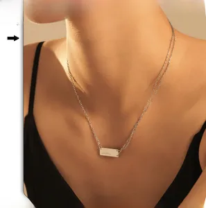 Close-up of a silver rectangular bar pendant with artistic engraving worn by a model