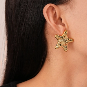 Close-up of a model wearing gold star-shaped earrings with unique hammered metal texture