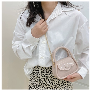 Detailed macro view of a mini beige patent leather handbag with gold chain and handle