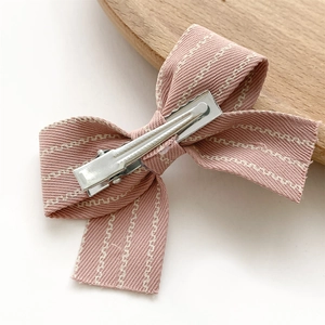 Detail of a pink fabric bow hair clip with white stitching and metal alligator clip