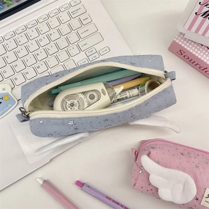 Close-up of pastel stationery bag with plush angel wings and silver stars on a white desk
