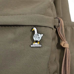 Détail d'un pin's en émail canard docteur sur un sac à dos vert avec gravure humoristique