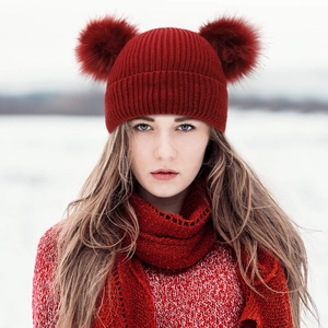 Close-up of red cable knit winter hat with double fur pom-poms and matching warm scarf