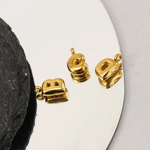 Gold bubble letter pendants B C D in polished stainless steel on a reflective base