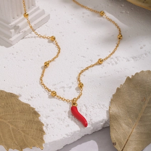 Macro detail of a gold beaded chain with a red chili pendant on a white stone surface