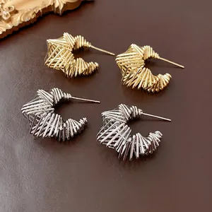 Gold and silver twisted C-shape hoop earrings with intricate woven texture on leather