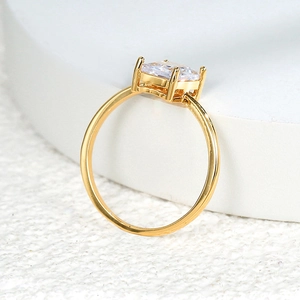 Minimalist gold ring with a square-cut sparkling gemstone on a white textured stand
