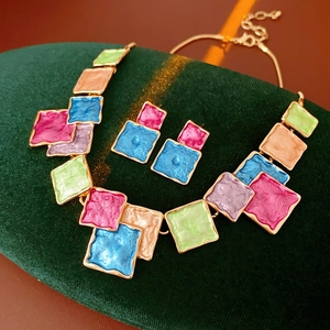 Detail view of colorful square enamel jewelry set on dark green velvet display stand