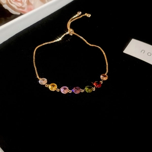 Detail of adjustable gold bracelet with seven colorful zircons on black velvet box