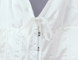 Détail d'un haut dos nu en satin blanc avec laçage et boutons sur le devant