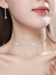 Close-up of a model wearing a shiny silver rhinestone heart necklace and earrings set
