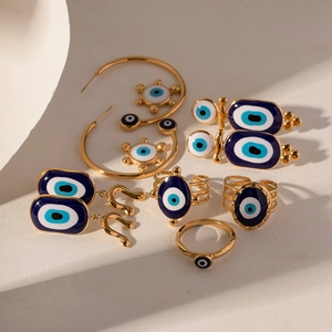 Golden Evil Eye jewelry set featuring blue pendant earrings and rings on beige background