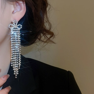 Detail of silver tassel earrings with diamond bow design worn by a model on a beige background
