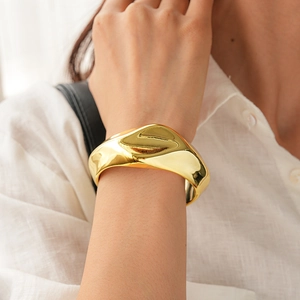 Detailed view of wide gold irregular fluid metal cuff bracelet on woman's wrist