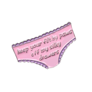 Macro view of pink enamel pin with keep your filthy paws off my silky drawers text