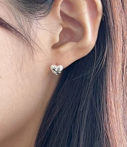 Close-up of heart-shaped silver stud earring featuring engraved star detail on model