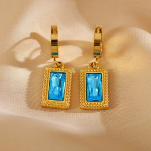 Detailed close-up of gold geometric earrings featuring sky blue rectangular zircons