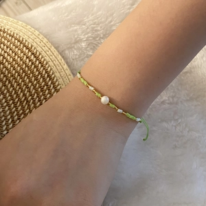 Macro detail of hand-woven green and white bead bracelet with a central pearl charm