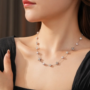 Close-up of a silver pearl necklace with clover charms on a model's neck