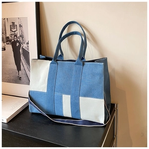 Detail of a patchwork denim tote bag featuring asymmetric beige canvas panels and a shoulder strap
